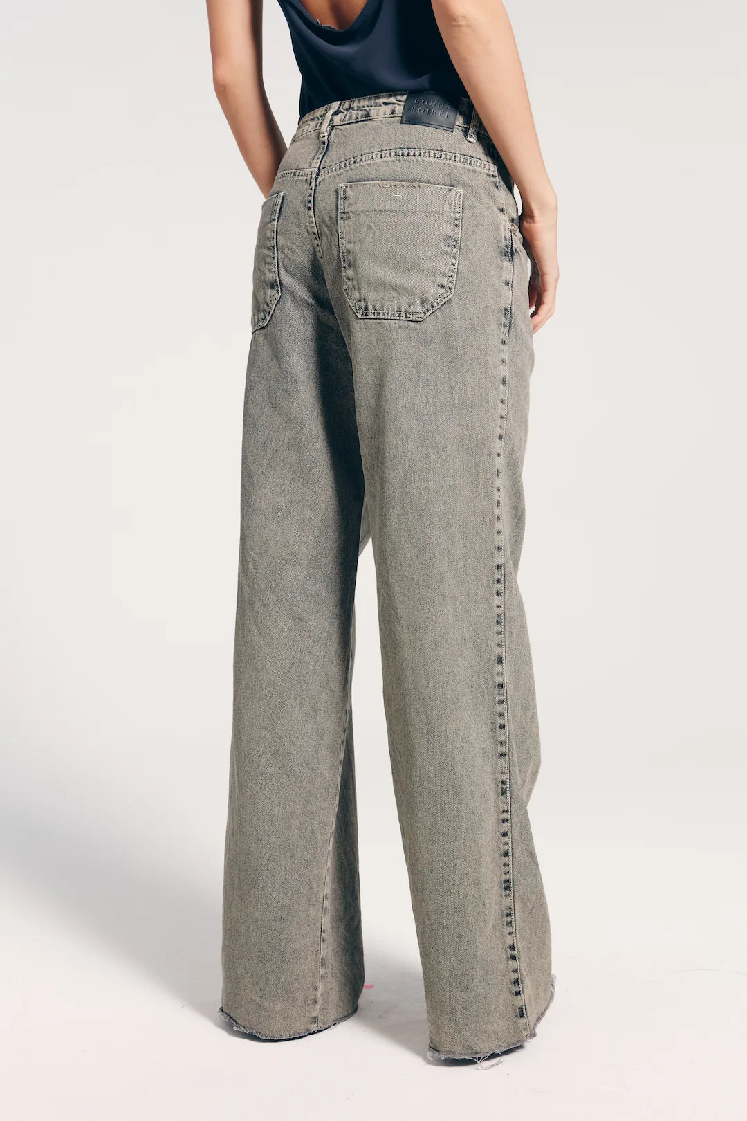 Calça jeans feminina reta cintura baixa vista de trás, com bolsos traseiros. A modelo veste também regata com as costas abertas.