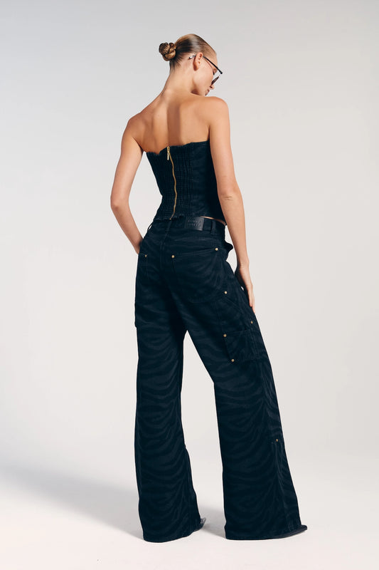 Parte de trás da calça jeans preta com rebites. A peça possui bolsos traseiros e ao longo de seu comprimento e passantes para cinto.