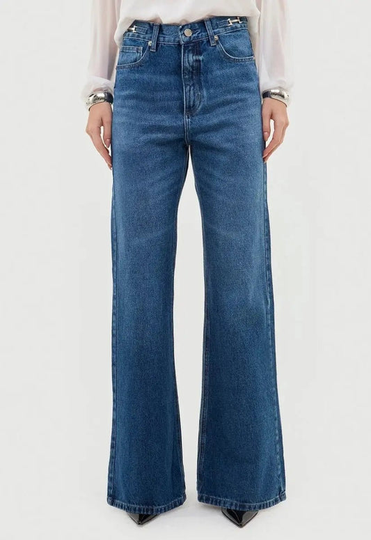 Modelo vestindo calça jeans wide leg azul. A peça é cintura alta e possui modelagem levemente flare.
