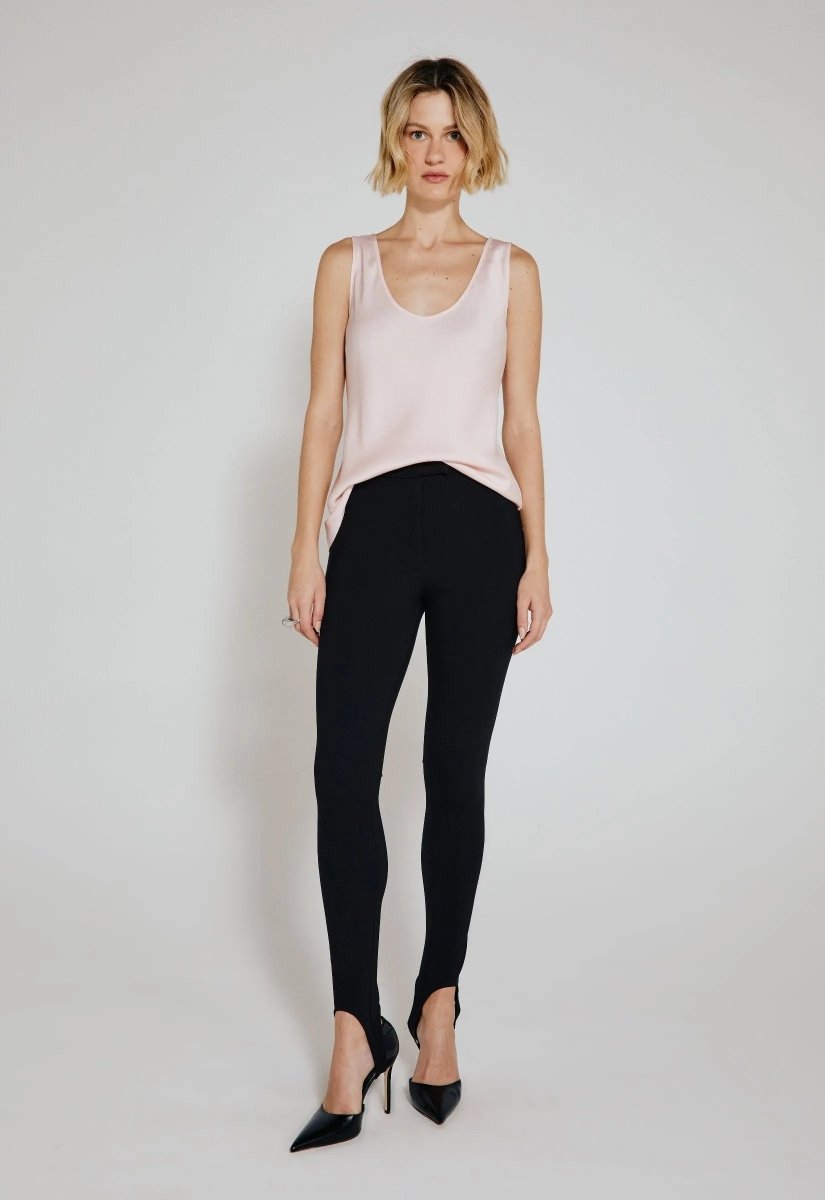 Modelo usando calça legging preta feminina com pezinho, combinada com blusa acetinada rosa claro e sapatos de salto preto.
