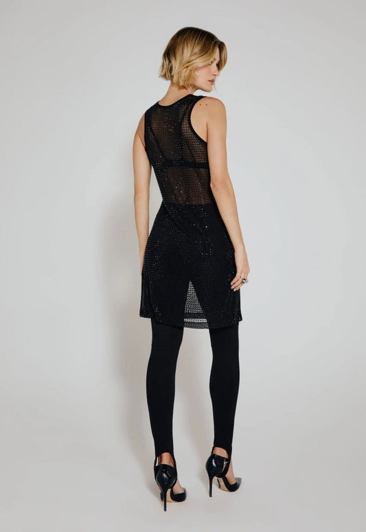 Modelo de costas vestindo calça legging preta feminina com pezinho, combinada com vestido curto transparente preto com brilho e salto alto preto.