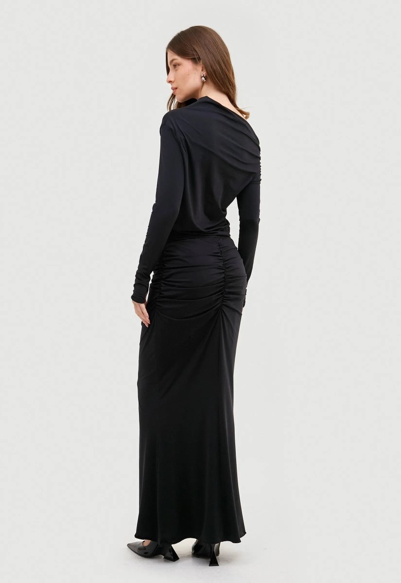 Saia longa preta drapeada, design elegante e fluido. Modelo combina a peça com blusa no mesmo estilo e salto preto.