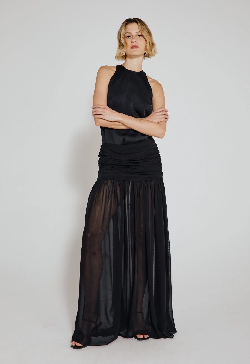 Mulher usando saia longa drapeada preta com transparência. O look combina tecido fluido e detalhes elegantes, oferecendo sofisticação e estilo moderno.