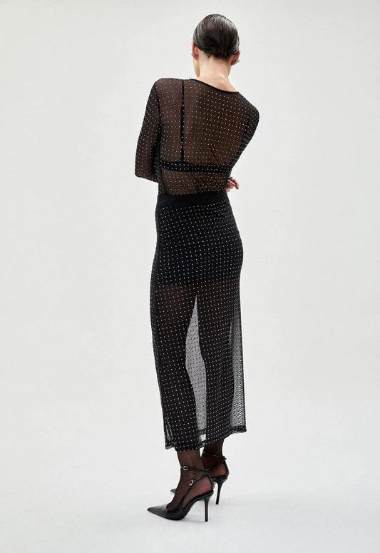 Saia tule preta com transparência e pequenos detalhes brilhantes. Elegante e moderna, combinada com blusa transparente e salto alto para um look sofisticado.