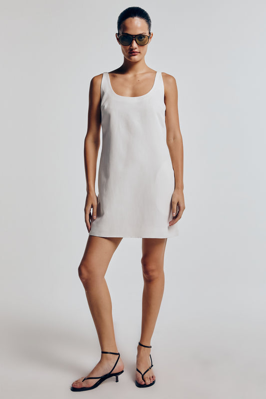 Modelo vestindo vestido linho feminino off white. A peça possui corte redondo no decote e é combinada com sandália preta. Modelo casual moderno.