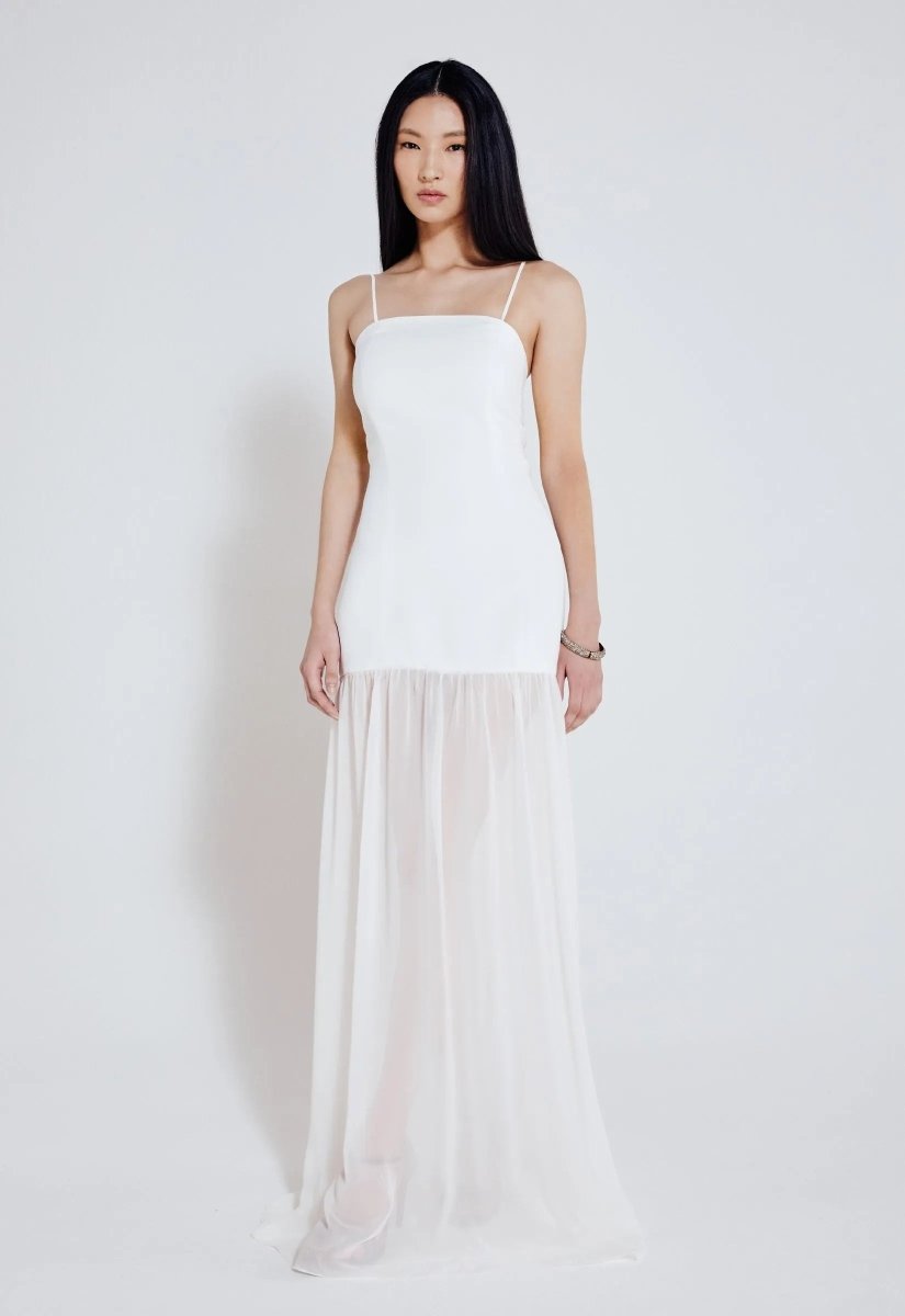 Mulher usando vestido longo off white com alças finas, busto ajustado e saia fluida com transparência. Look elegante e minimalista.