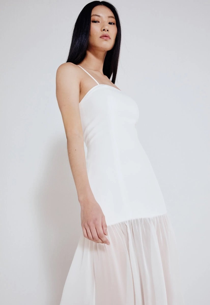 Mulher usando vestido longo off white com alças finas e saia leve e fluida. Look elegante e minimalista, perfeito para ocasiões sofisticadas.