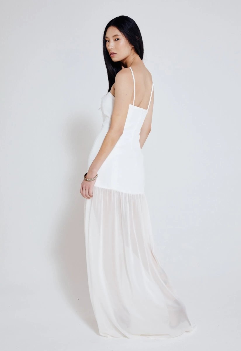 Mulher usando vestido longo off white com alças finas, busto ajustado e saia fluida transparente. Look elegante e minimalista.