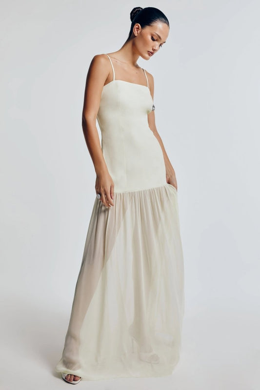 Vestido longo verde claro, alças finas e saia esvoaçante. Fundo neutro destaca a elegância e suavidade do tecido.
