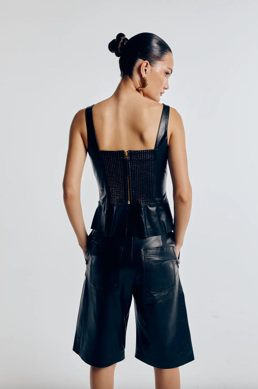 Mulher usando bermuda feminina couro preta, modelagem reta e bolsos laterais, combinada com top e acessórios dourados.