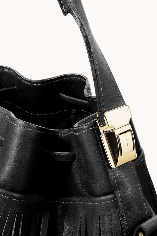 Close da bolsa de couro feminina média preta. Detalhe de fivela dourada na alça.