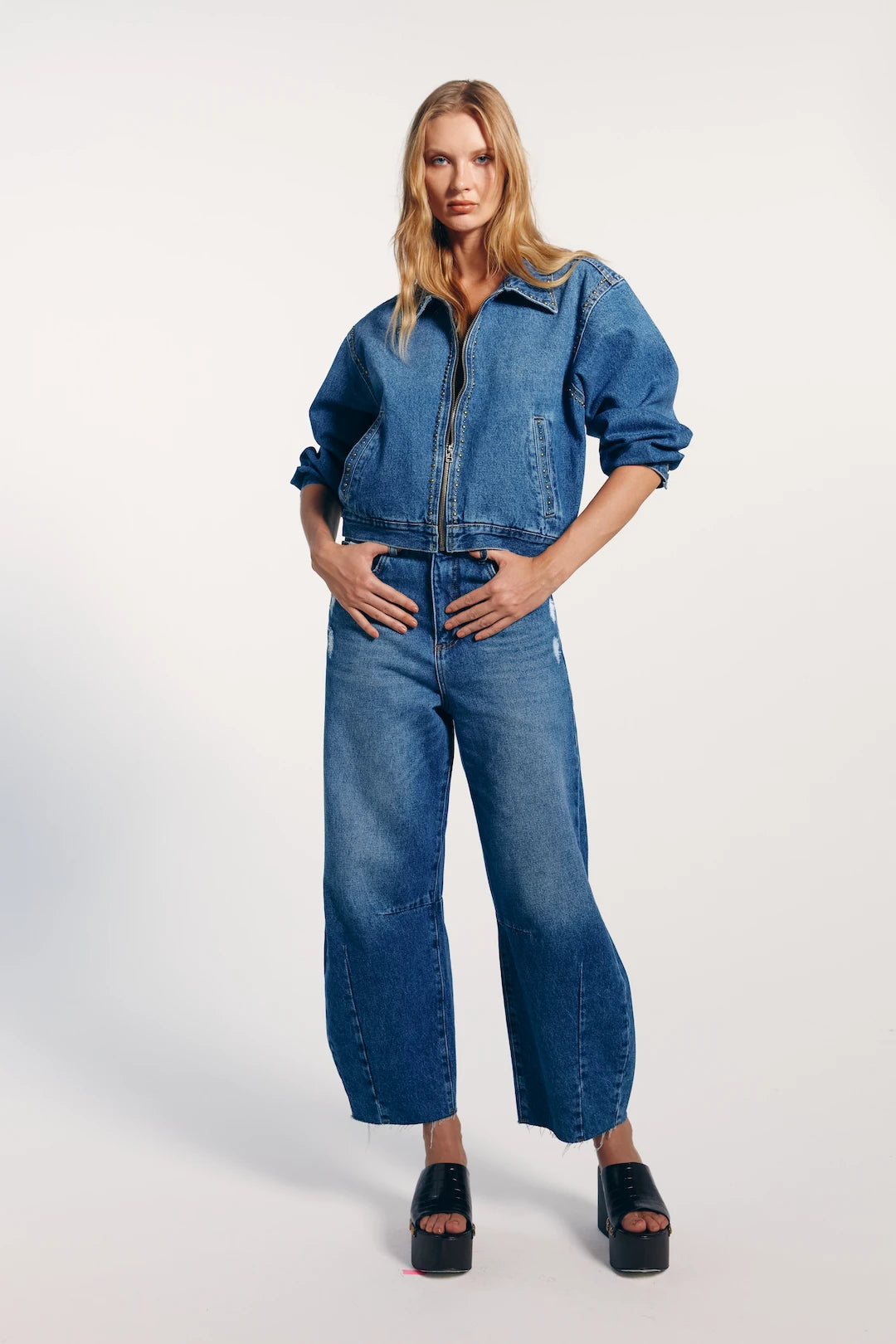 Modelo vestindo a calça jeans barrel combinada com jaqueta jeans. O look transmite modernidade e conforto.