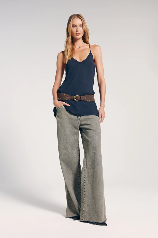 Modelo vestindo a calça jeans feminina reta cintura baixa. Ela combina a peça com regata azul marinho e cinto marrom com detalhes dourados. O look é estiloso e moderno.