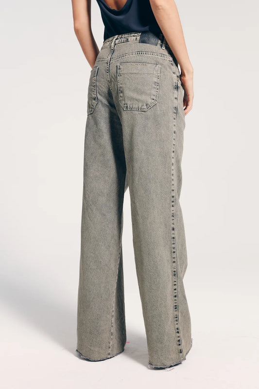 Calça jeans feminina reta cintura baixa vista de trás, com bolsos traseiros. A modelo veste também regata com as costas abertas.