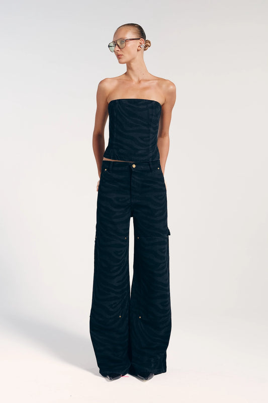 Modelo vestindo a calça jeans preta com rebites, da Bonne Soirée. A peça possui estampa de zebra, garantindo um visual com muita personalidade.