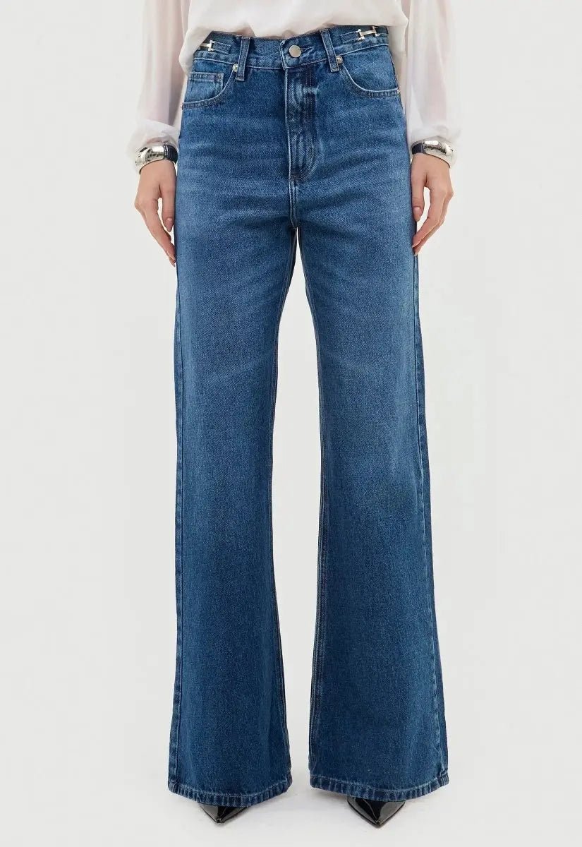 Modelo vestindo calça jeans wide leg azul. A peça é cintura alta e possui modelagem levemente flare.