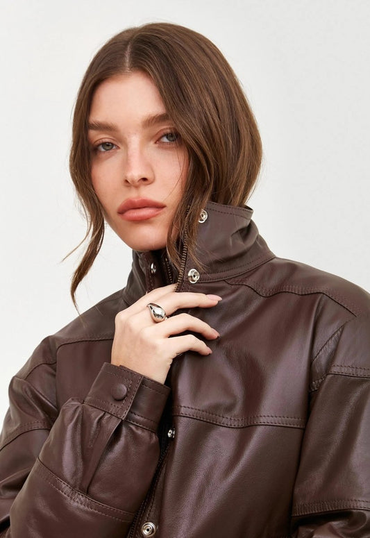 Mulher usando a jaqueta bomber marrom com acabamento em couro. A peça possui botões prateados, gola alta e estilo moderno, formando um look elegante.