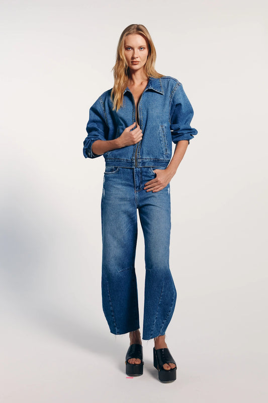 Modelo vestindo jaqueta jeans feminina trucker, combinada com calça jeans e sapato preto. Peça versátil e atemporal.