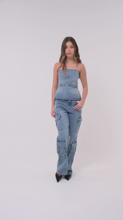 Modelo veste corset jeans com botões dourados na parte de trás. A peça é combinada com calça cargo jeans e scarpin preto.