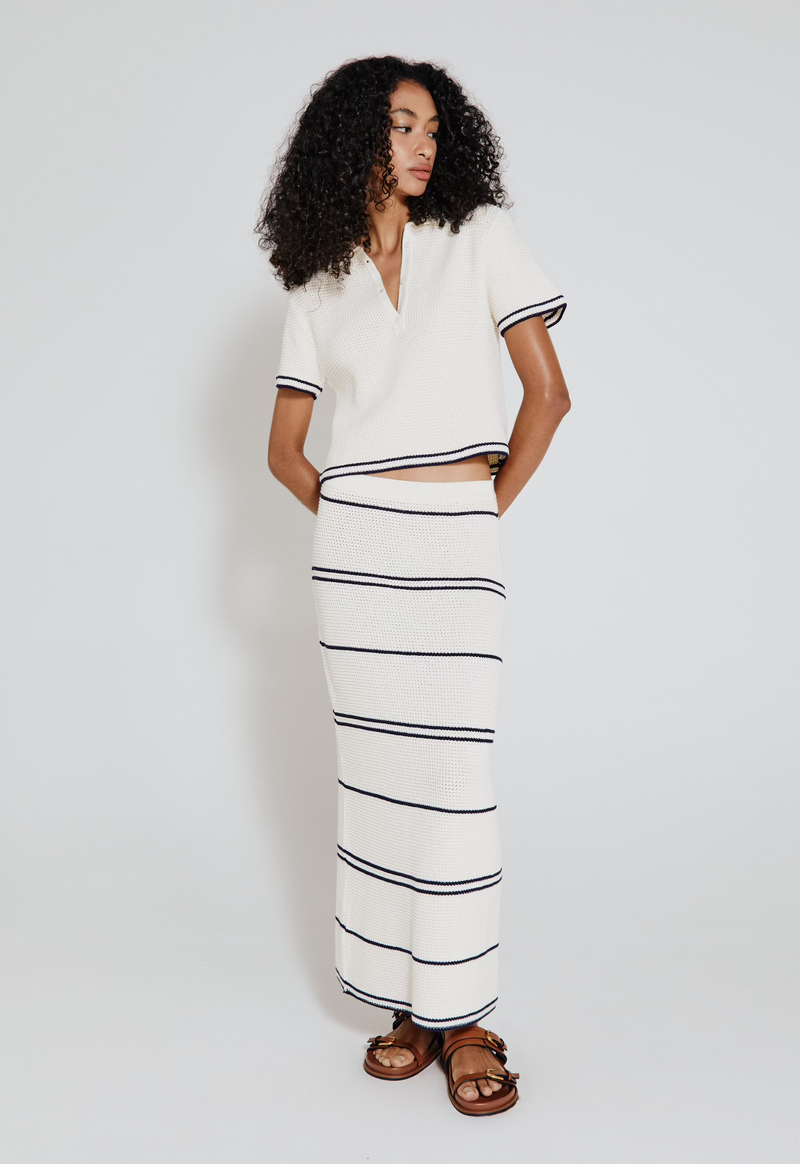 Modelo vestindo saia listrada tricot off white, a peça é branca com detalhes em azul marinho.