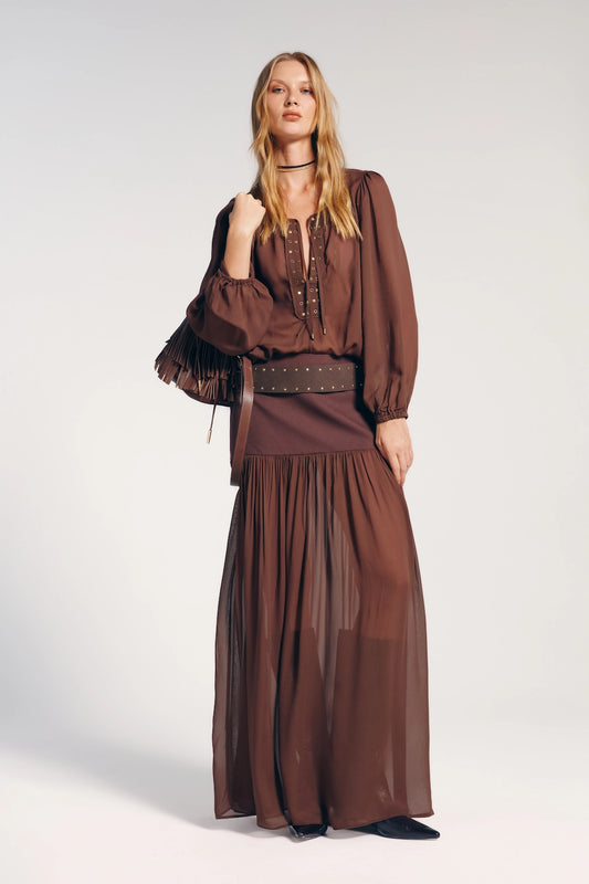 Saia longa marrom boho, perfeita para um visual descontraído e versátil. Na imagem  modelo combina com bolsa de franjas.