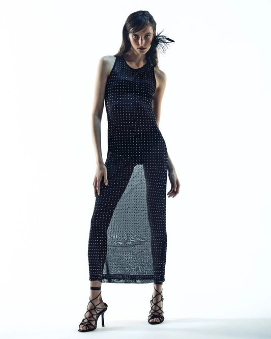 Modelo vestindo vestido longo nadador preto, com tecido translúcido e detalhes de aplicações brilhantes, combinado com sandálias de tiras pretas.