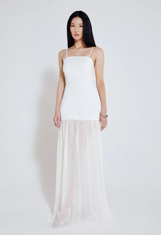 Mulher usando vestido longo off white com alças finas, busto ajustado e saia fluida com transparência. Look elegante e minimalista.